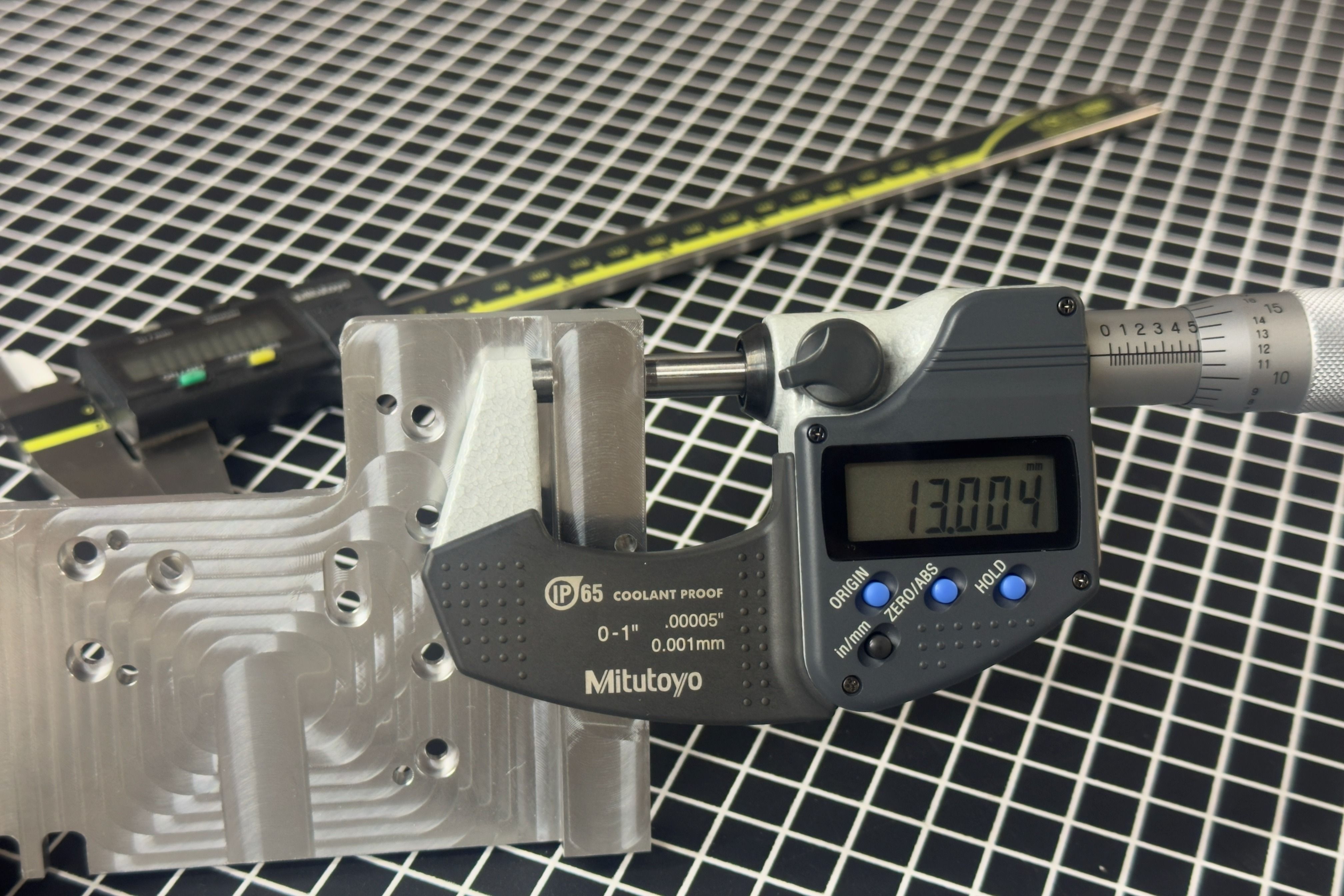 Machined aluminum part being measured with a digital micrometer